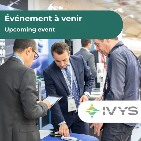 Promotional graphic for an upcoming event. Three attendees in business attire stand around a trade show booth, looking at a tablet and equipment on a table. A green banner at the top reads “Événement à venir / Upcoming event.” The IVYS logo appears in the lower right corner. The background shows a busy exhibition hall with displays and signage.